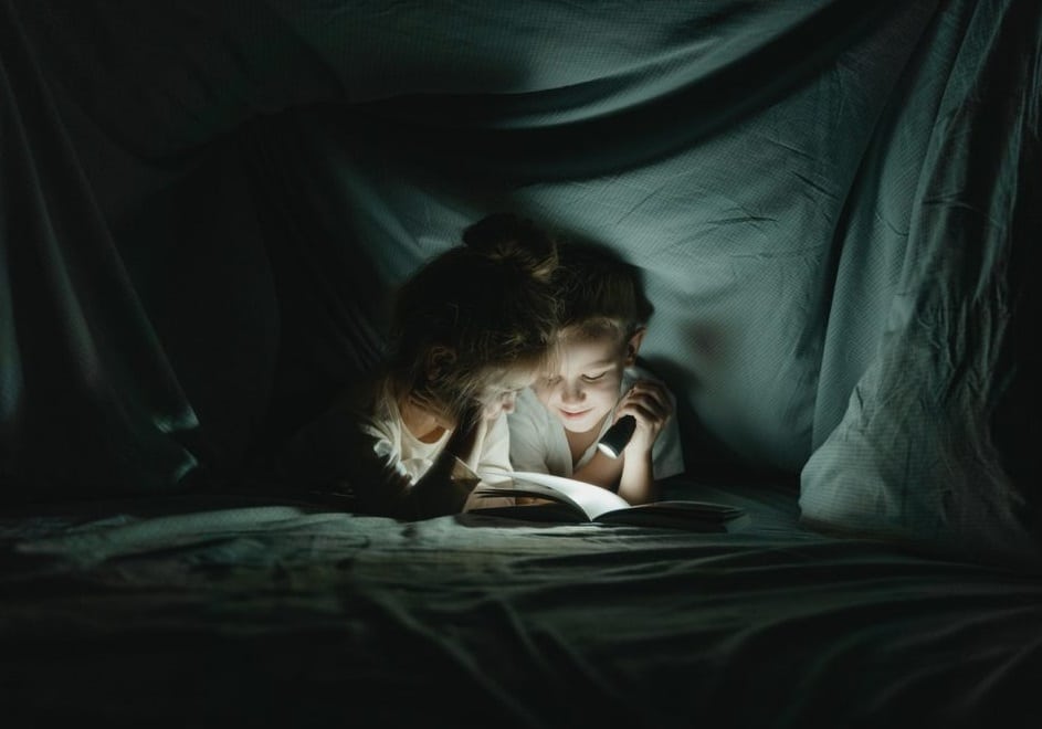 2 filles lisant un livre à la lampe torche dans une cabane de tissu